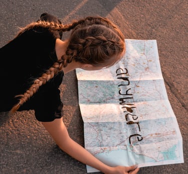 Young girl in braids laying down on road while she looks at map.