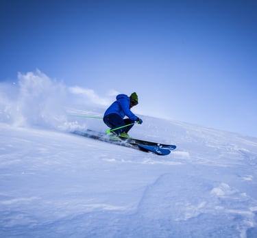 Un esquiador con chaqueta azul se abre paso entre la nieve polvo en una empinada ladera de montaña 
