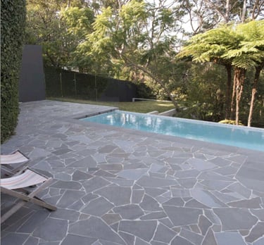 Crazy Paving - Stone patio with two lounge chairs beside a rectangular pool surrounded by lush trees