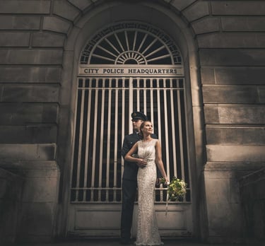A bride in a white gown and a groom in a police uniform pose outside City Police Headquarters.