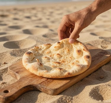 Close-up of a hand placing a freshly baked pita bread on a rustic wooden board, warm golden-hour sunlight casting soft shadows, sand-beige table background, 35mm photography