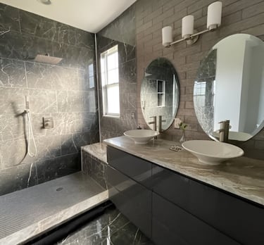 Modern bathroom featuring dark marble tiles, a walk-in shower, and a double vanity with vessel sinks.