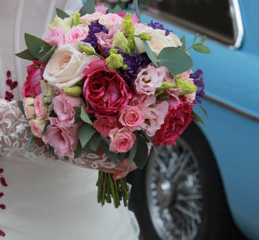 Mariée qui tient un bouquet de fleurs avec en arrière-plan une voiture bleue de collection