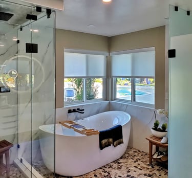 Elegant and bright master bathroom with marble wall, freestanding tub, and glass shower and toilet enclosures.