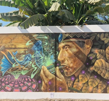 Mural painting of an indigenous shaman with a tobacco pipe and mystical spirit figures under banana leaves.