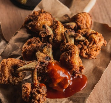 Alitas y muslitos de pollo fritos crujientes, cubiertos con una capa dorada y bañados con salsa