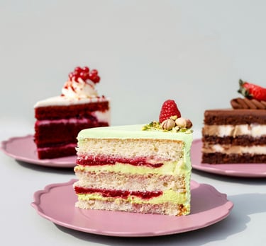 Rebanadas de pastel de pistache con frambuesa, red velvet y chocolate sobre platos rosas