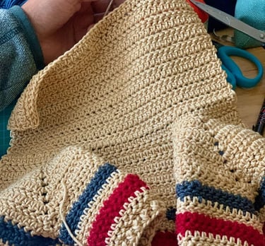 Tejiendo a mano un suéter beige a crochet con puños y dobladillo a rayas en rojo, blanco y azul