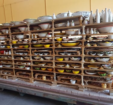 Handmade ceramic pottery and painted bowls drying on wooden racks in an Italian artisan workshop.