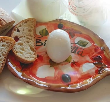 Fresh mozzarella cheese ball on a decorative ceramic board with slices of crusty Italian bread.