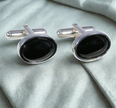 Elegant oval black onyx cufflinks set in sterling silver on a luxury silk fabric background.