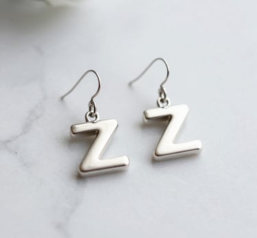 Delicate silver earrings with jade green details, photographed against a muted green background.