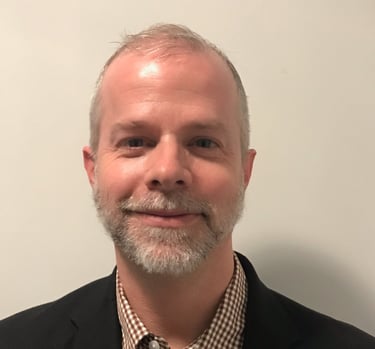 Alexander Slagg with grey beard, black sport coat, checkered button down shirt