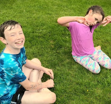 Two happy kids sitting on green grass playing outside while covered in dirt and mud.