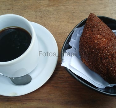 [Download] Uma xícara de café fumegante sobre um pires branco e num pratinho, um kibe dourado...