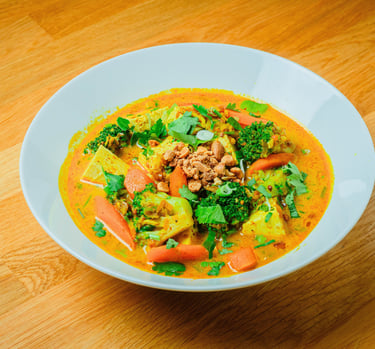 Bowl of vietnamese curry with broccoli, carrots and herbs topped with crushed peanuts on a wooden t