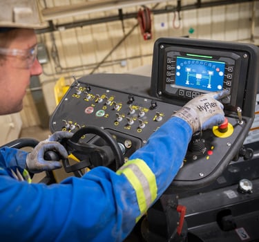 A heavy equipment technician is inspecting the hydraulic settings on a Bomag paving machine's digital dashboard 