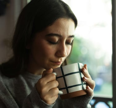 A young woman peacefully holding a ceramic mug while enjoying a hot cup of coffee or tea indoors.