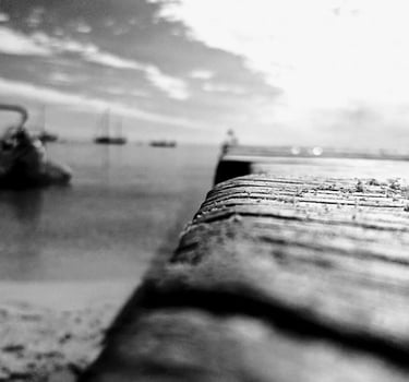 a black and white photo of a pier with boats in the background