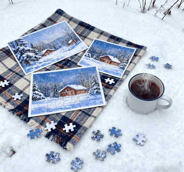 There is a cup of coffee and a completed jigsaw puzzle on the snow.