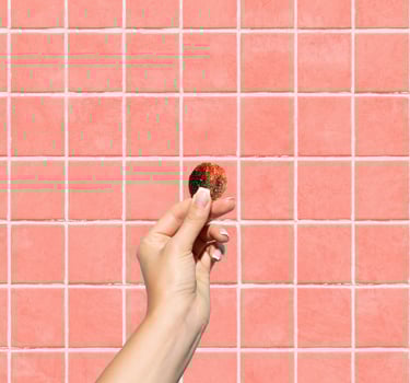 A hand holding a round piece of gummy against a pink tiled wall background.