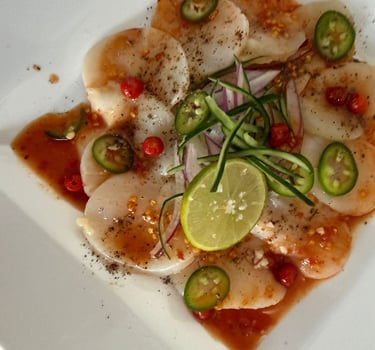 Aperitivo de carpaccio de vieira fresca con lima, rodajas de jalapeño y salsa de chile, servido.