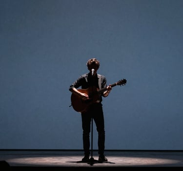 A singer-songwriter performing on a minimalist stage in a Latin American / Spanish concert hall, silhouette against a muted indigo background, professional cinematic lighting.