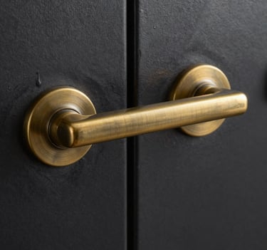 A macro shot focusing on a custom-made brass door handle integrated into a black steel frame. The craftsmanship is evident in the brushed texture of the warm bronze metal against the deep charcoal steel.