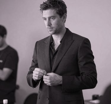 A candid black and white style photograph with deep charcoal and pale lavender mist tones, showing Stefan Taylor preparing backstage. He wears a tailored suit, looking authoritative and focused before a show.