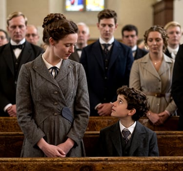 A young boy and woman in Victorian era period clothing sitting in a church pew during a formal service.