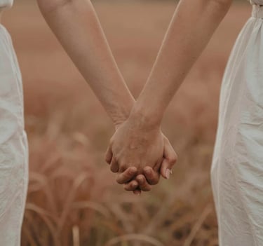 A close-up of a couple's hands interlaced while walking through a field, shot in warm cinematic light with natural focus, incorporating soft terracotta and sand tones in the environment.