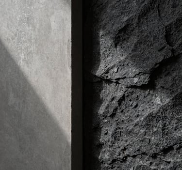 A close-up, high-fashion style shot of architectural materials. Smooth light gray concrete meeting textured dark charcoal stone. Dramatic side-lighting creates a high-contrast, moody aesthetic in a South American / Brazilian luxury home.