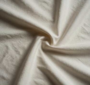 An abstract photographic study of light and shadow on a wrinkled soft off-white fabric, creating deep charcoal folds and sophisticated textural depth.
