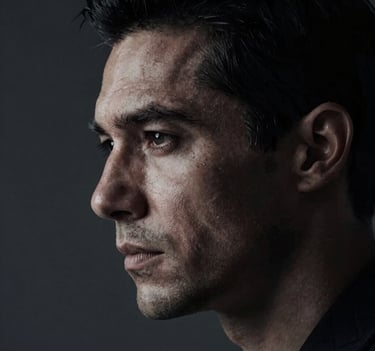 A close-up dramatic portrait of a male actor in profile, half-submerged in shadow. Hard cinematic lighting highlighting the texture of the skin. Dark palette with #0F0F0F and #333333 tones.
