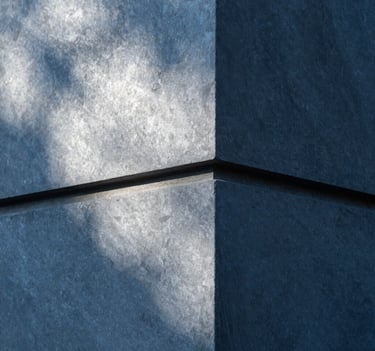 Close-up of an architectural detail featuring slate blue concrete and sharp edges. Light and shadow create a geometric pattern of soft cloud white and deep obsidian. Industrial and premium feel.