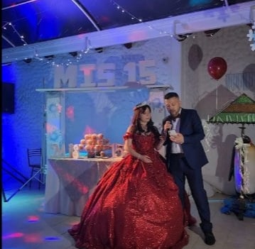 Quinceañera con vestido rojo junto a su padre, mesa de dulces y decoración elegante.
