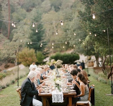 Dîner en plein air sous guirlandes lumineuses dans un jardin, longue tablée conviviale décorée 
