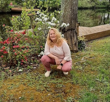 Claudia Smarkola, healer and teacher in a pink sweater and pants casually squatting down