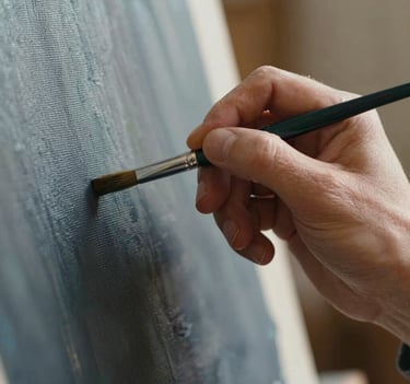 An extreme close-up of a painter's hand holding a fine brush, delicately touching a canvas. The lighting is soft and warm, highlighting the texture of the skin and the woven canvas. Shadows are deep using #1A1A1A, with hints of #6B705C on the brush handle.