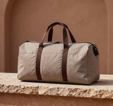 Minimalist product photography of a premium 100% cotton hand-quilted duffle bag in soft taupe with deep espresso accents, placed on a rustic stone ledge. Warm clay and earthy brown backdrop. Clear day lighting, premium quality look for Global Premium / North American and European Retailers.