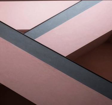 An interior architectural shot of a staircase in a modern US building. The railing creates a series of diagonal lines that divide the frame into geometric segments. The palette includes soft pink and charcoal gray tones, emphasizing a minimalist and artistic mood.
