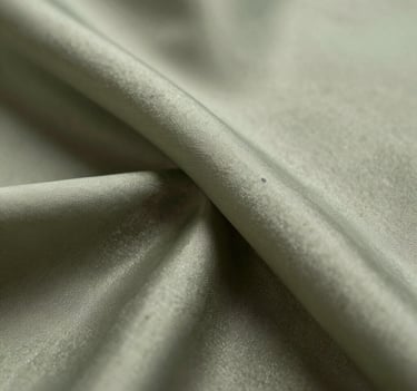 A macro photograph focusing on the intersection of two silk layers. The light passes through the muted olive and pale sage fibers, creating a biological, membrane-like appearance with a soft, ethereal glow.