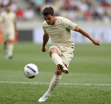 A mid-action shot of a football player mid-kick, muscles tensed, ball in motion with a slight blur. Professional lighting, vibrant yet natural, incorporating the brand's earthy tones #8C847E in the grass and #F2F1ED in the kit.