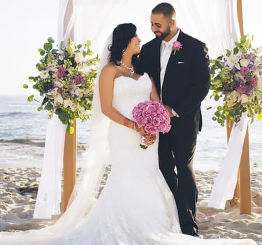 bride and groom standing under floral decorated arbor on the beach