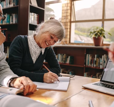 Personas mayores realizando ejercicios de estimulación cognitiva en grupo, escribiendo en cuadernos 
