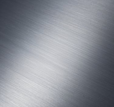 Close-up photography of a brushed metal surface showing fine, elegant texture. Professional studio lighting with cold, silvery tones. Minimalist and refined Northern European style.