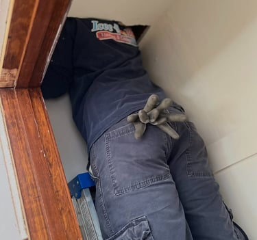 Professional HVAC technician on a ladder inspecting home ceiling ductwork and insulation.