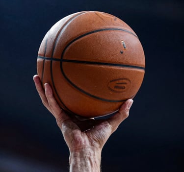 Close-up action photography of a basketball player's hand gripping a ball mid-dunk. Dark blue background with moody shadows, sharp focus on skin texture and the leather of the ball, high-energy professional sports aesthetic, Western / International.