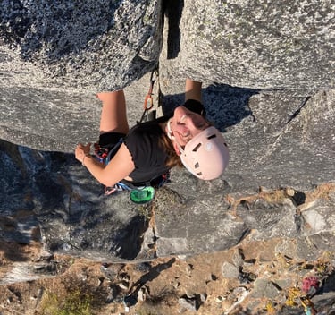 A smiling person climbing a rock face