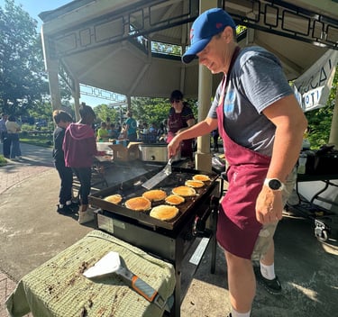 Kids in the background of a person flipping pancakes on a griddle in a park